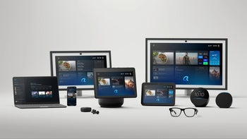 A collection of Amazon devices, including smart displays, a laptop, a phone and smart glasses, arranged on a white surface.