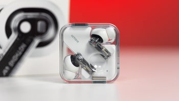 Nothing Ear placed on a white table in their charging case, with their charging box visible in the background.