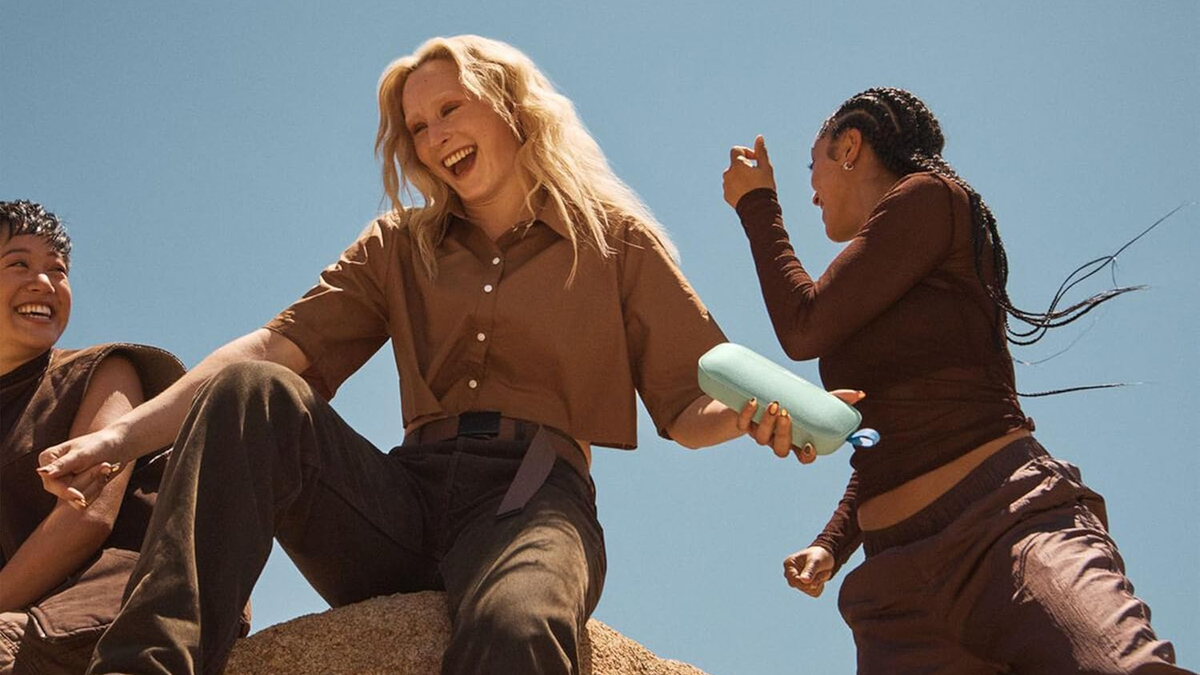 A girl holds the Bose SoundLink Flex 2nd Gen in her hand while having fun with friends outdoors.
