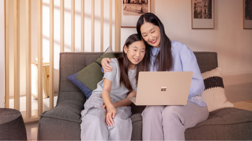 A person and a child looking at a laptop together on a couch.