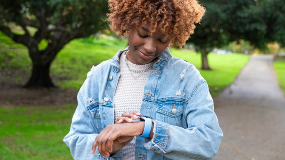 A photo of a person looking at their smartwatch outdoors in a park.