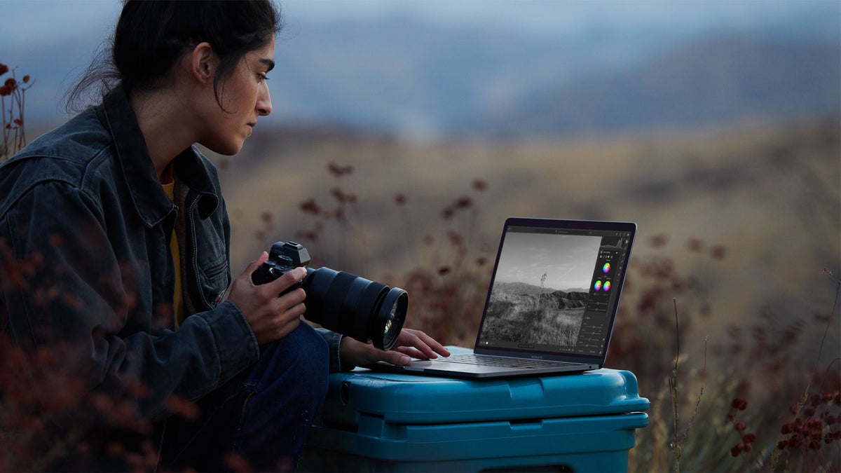 A person edits a black-and-white landscape photo on a MacBook outdoors.
