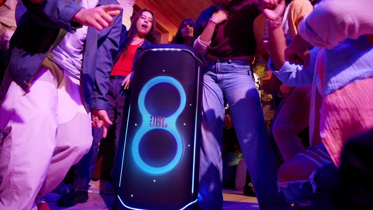 A party scene with people dancing around a JBL Partybox Ultimate glowing with blue lights.