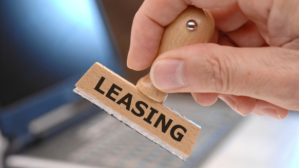 Hand holding a wooden stamp that says "leasing" on it.