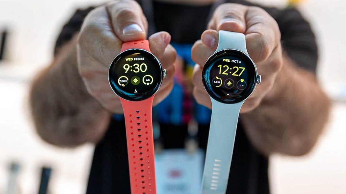 Two hands holding two smartwatches by the end of their wrist bands.