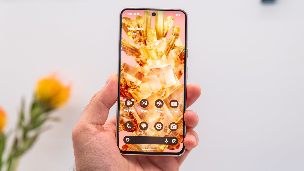 A person holds the Pixel 8 against a light background, with a flower visible in the background.