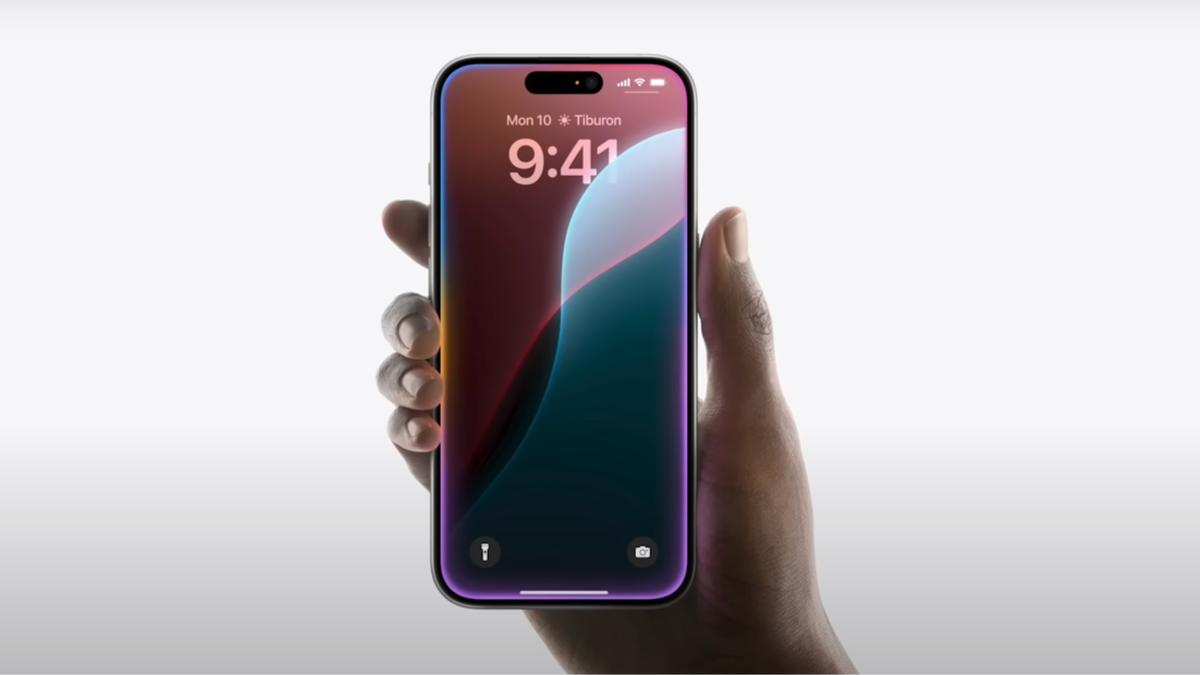 A hand holding an iPhone with the home screen on the display.