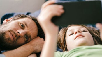 Father and child lay on bed watching a phone's screen.