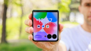 Out of focus man holding folded flip phone with cover display turned on.