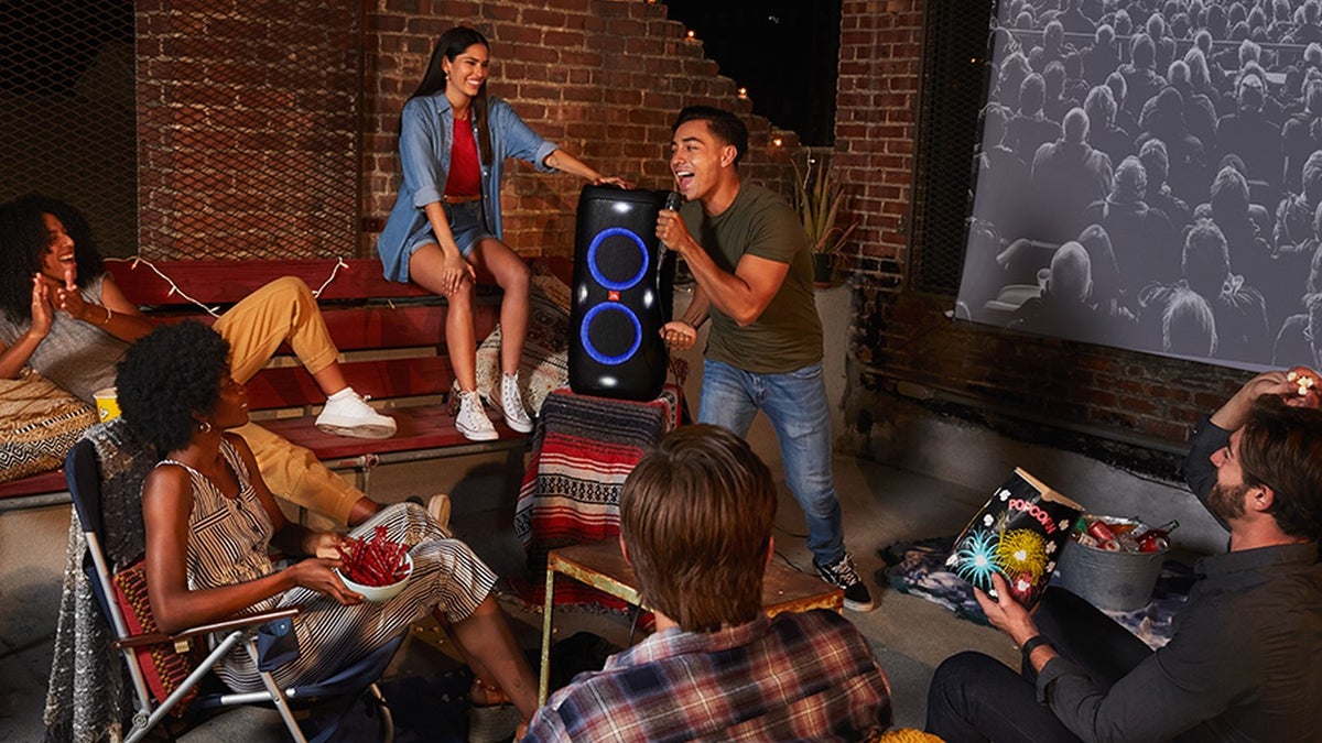 A group of people are enjoying an outdoor movie night, with snacks, drinks, and a speaker for enhanced audio.