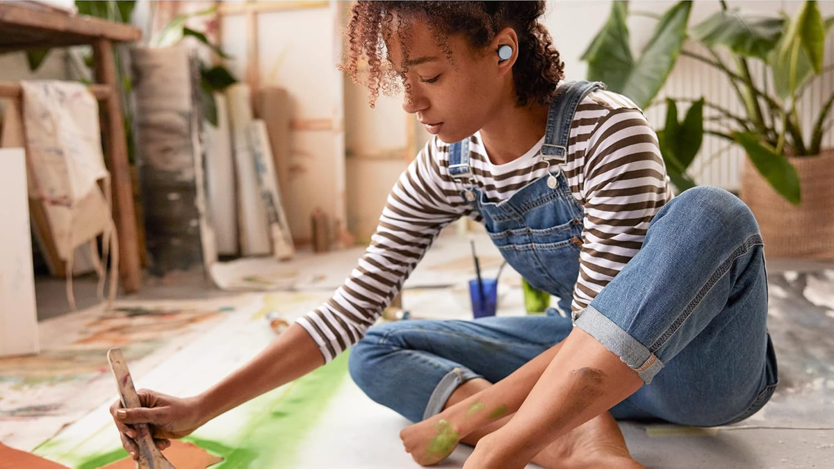 A woman wears the Pixel Buds A Series while painting in an indoor environment.