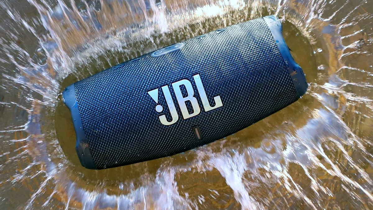 JBL Charge 5 on sand with water splashes around it.