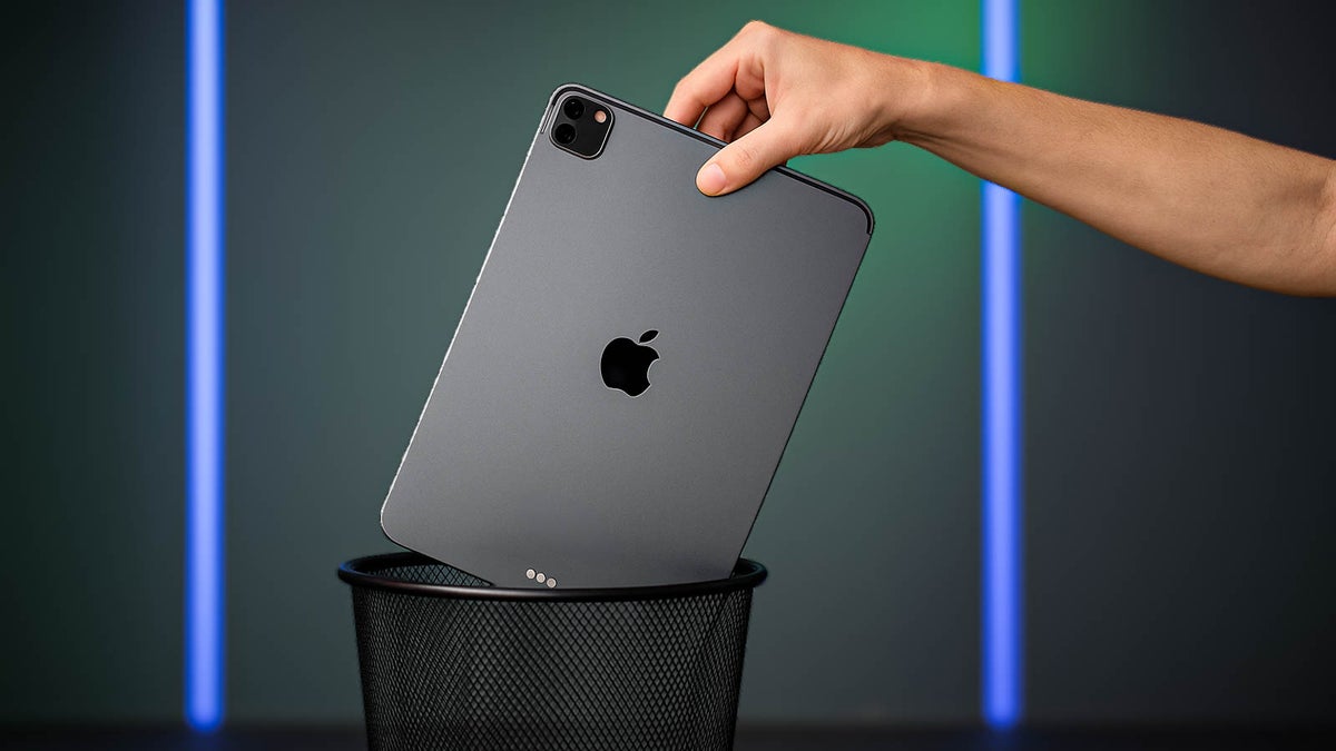A hand drops a space gray iPad Pro into a black mesh trash can.