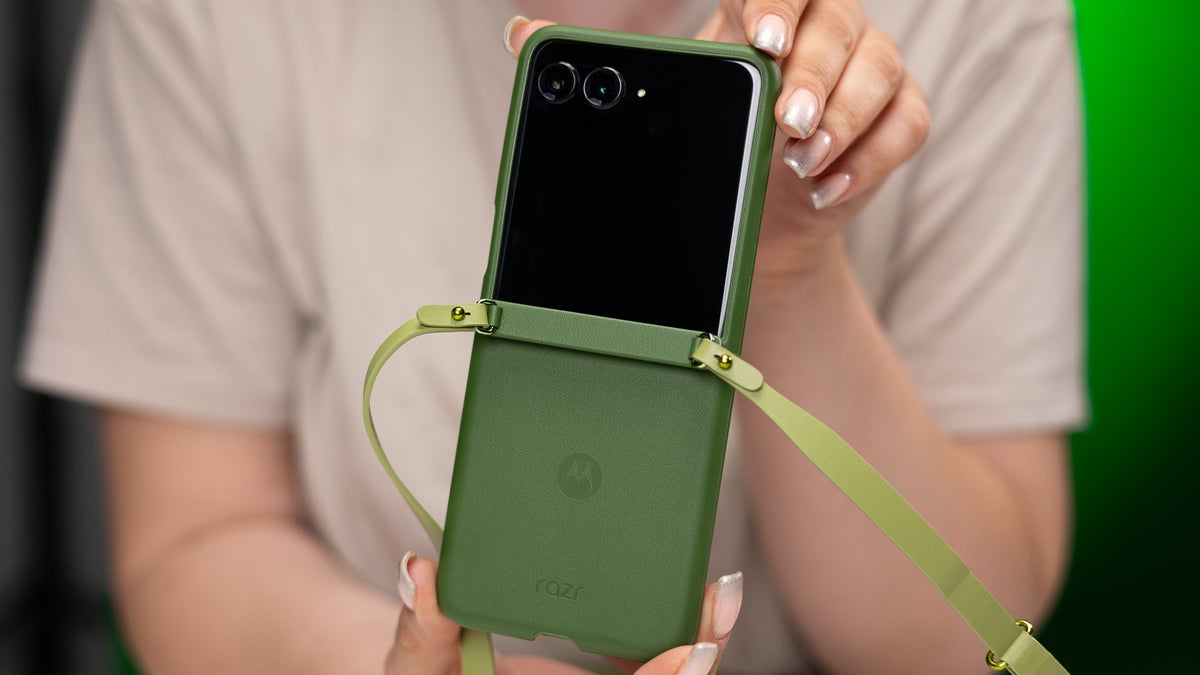 A woman holds the Motorola Razr+ (2024), which has a matching strap case attached.