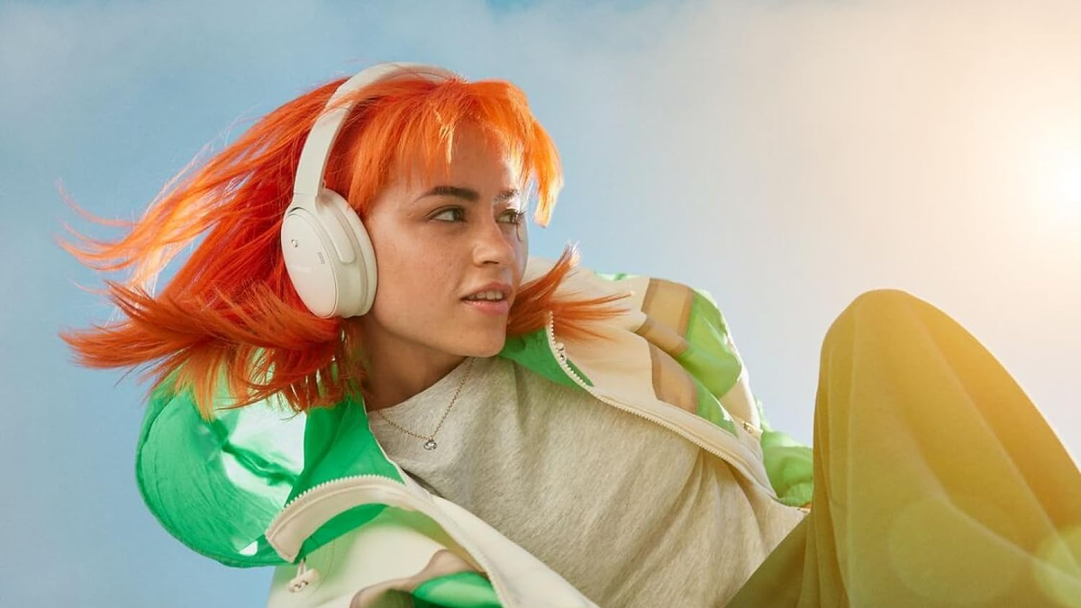 Person with orange hair wearing over-ear headphones and colorful clothes, enjoying music in a dynamic pose.