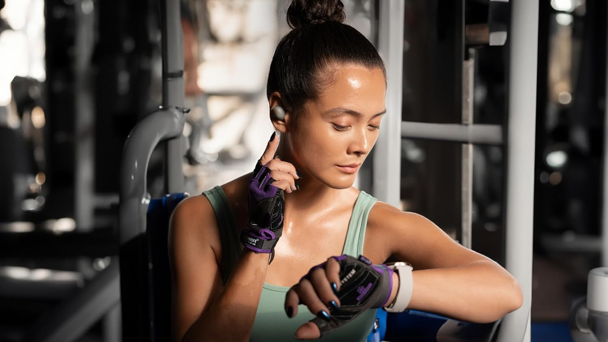 A woman is raising her arm to touch the Sennheiser Momentum Sport earbuds while working out.