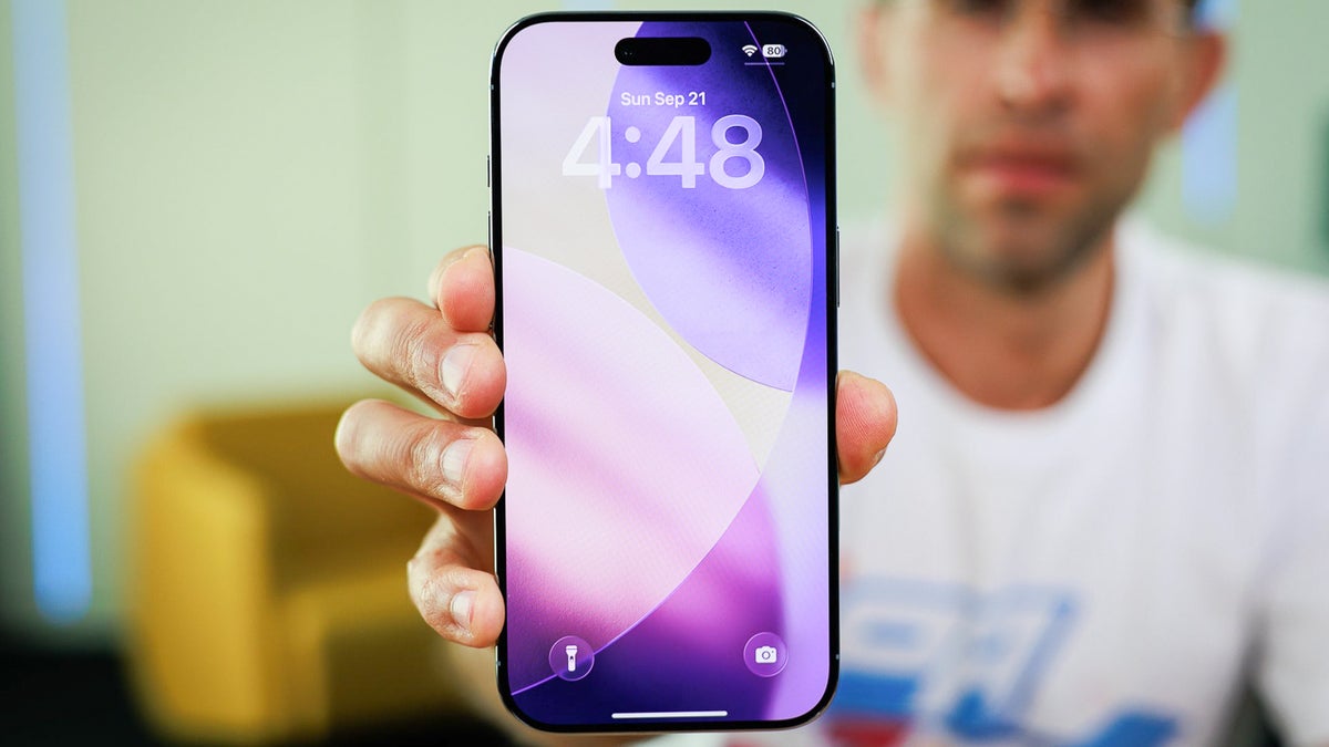 Person holding an iPhone showing its lock screen with a purple-themed wallpaper.