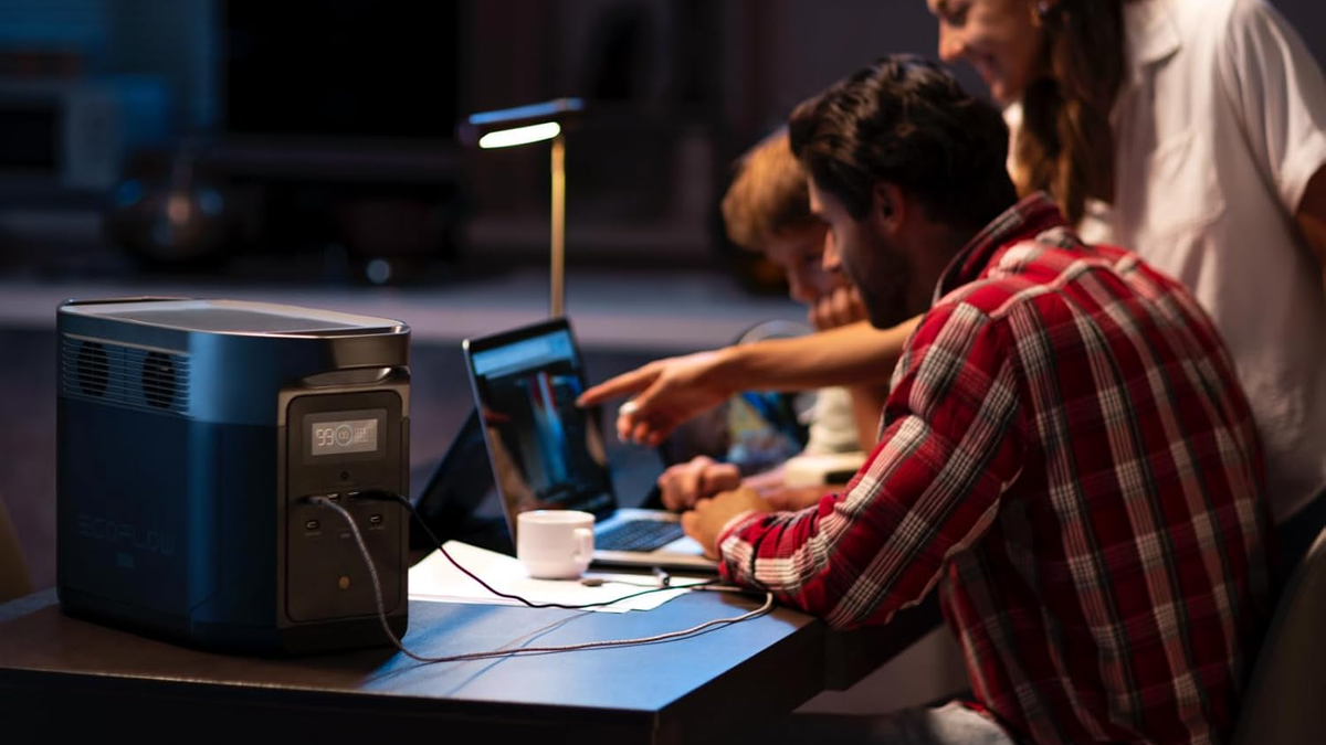 EcoFlow Delta 2 Max on a table, with equipment plugged in and people visible in the background.