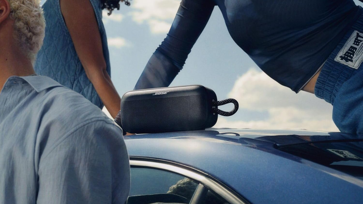 A Bose SoundLink Plus speaker on the roof of a car, with people surrounding it.