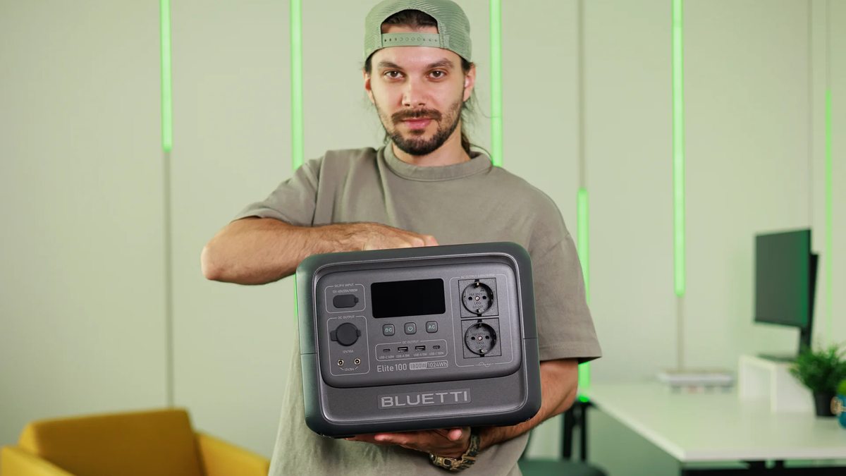 A person holds the Bluetti Elite 100 v2, showcasing its front design with LCD display and multiple outlets.