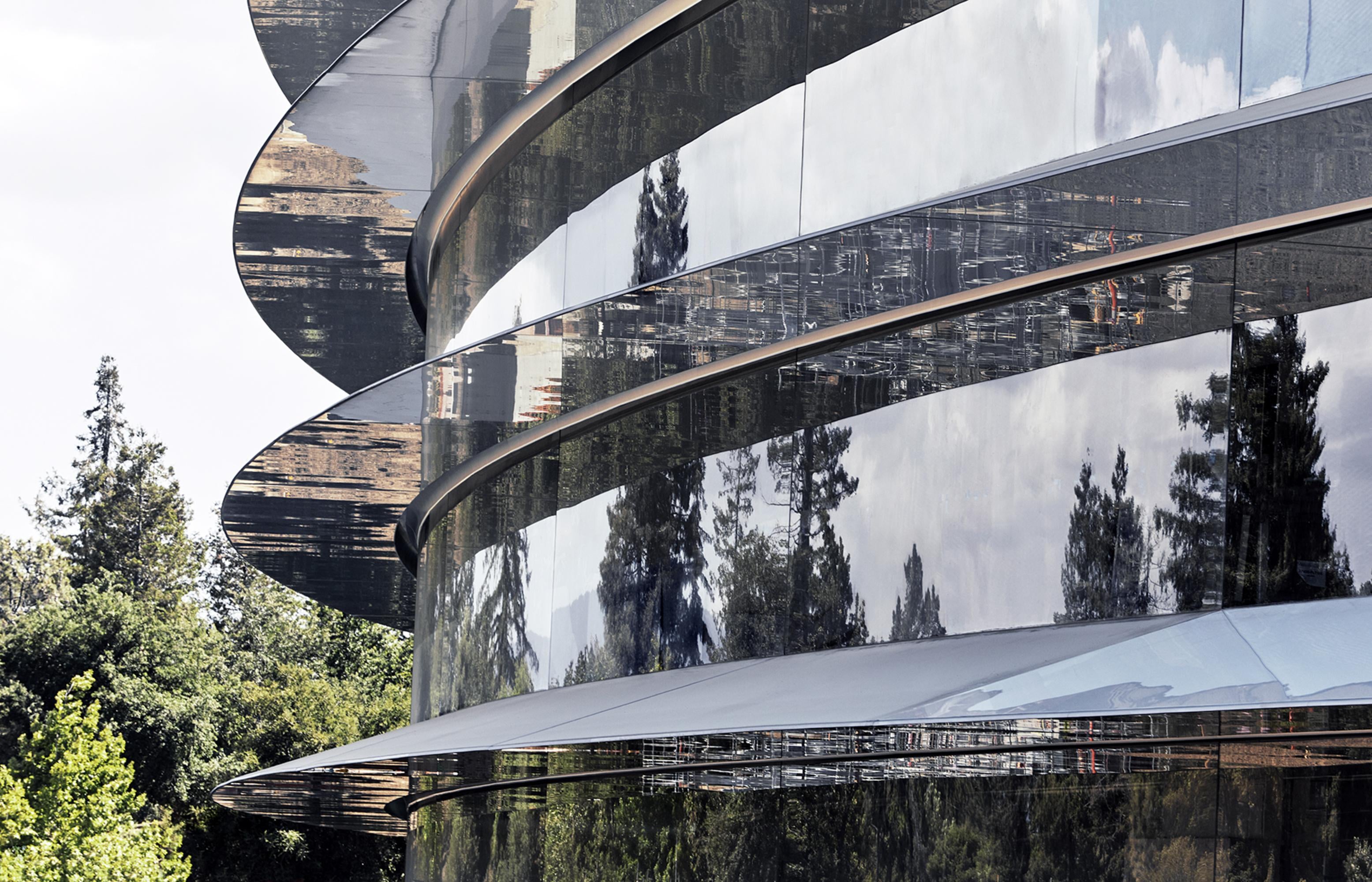 Curved glass encompassing the ring-shaped building reflects the surrounding vegetation. - All future Apple products will come from this amazing new office building