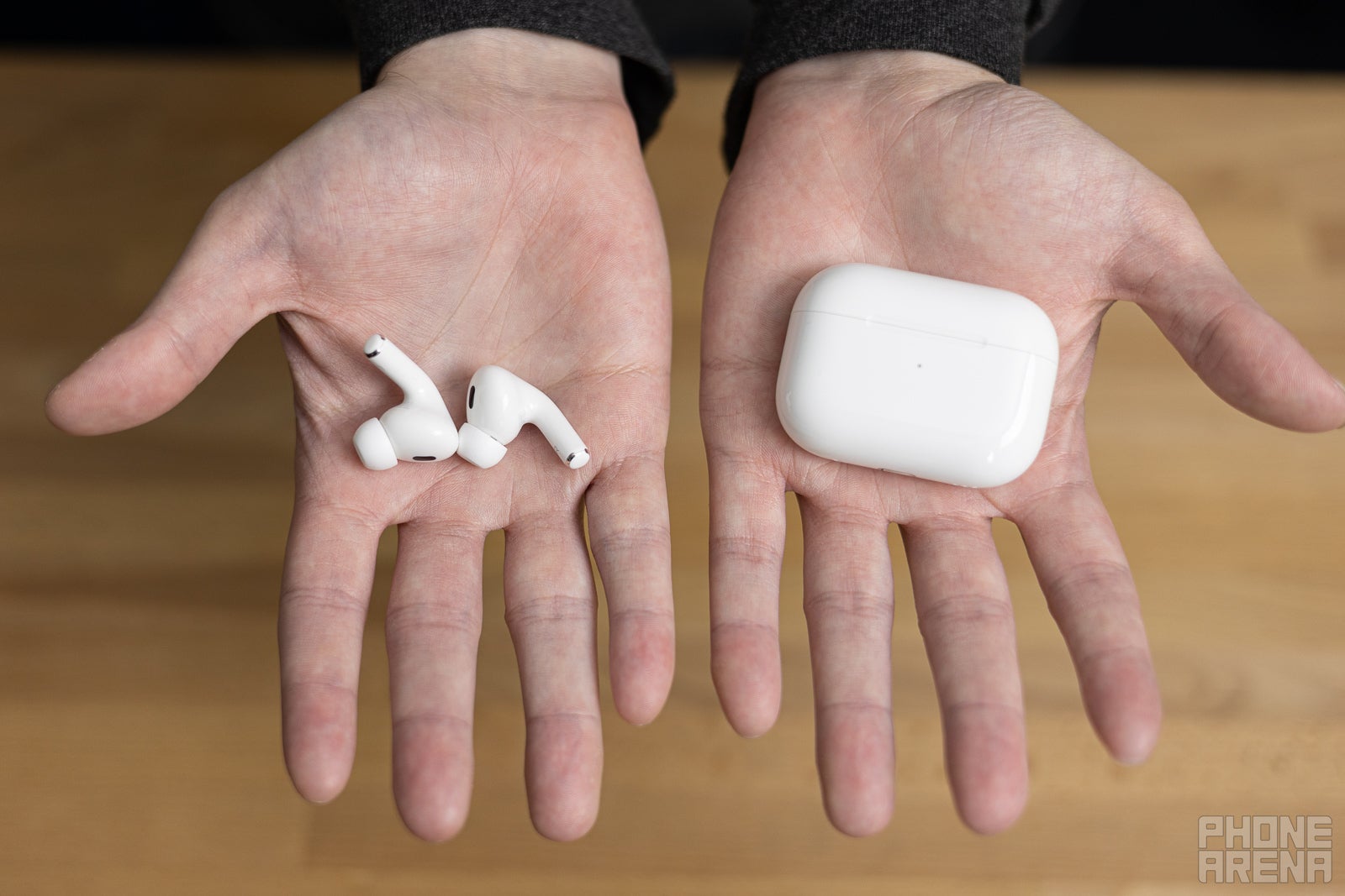 AirPods Pro 2 held in a person&amp;#039;s hands against a wooden table background.