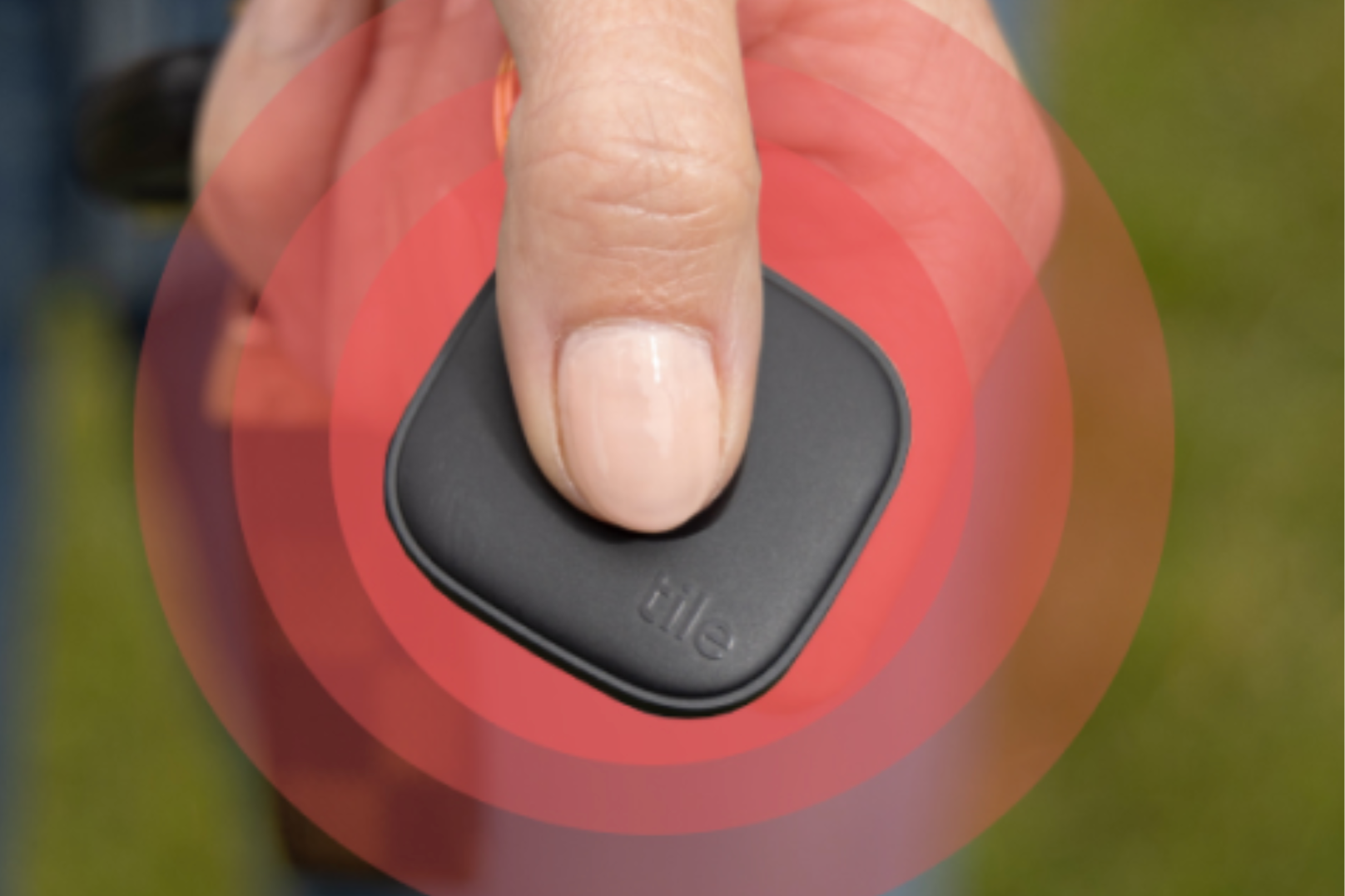 A person presses an SOS alert button on a Tile Bluetooth tracker.