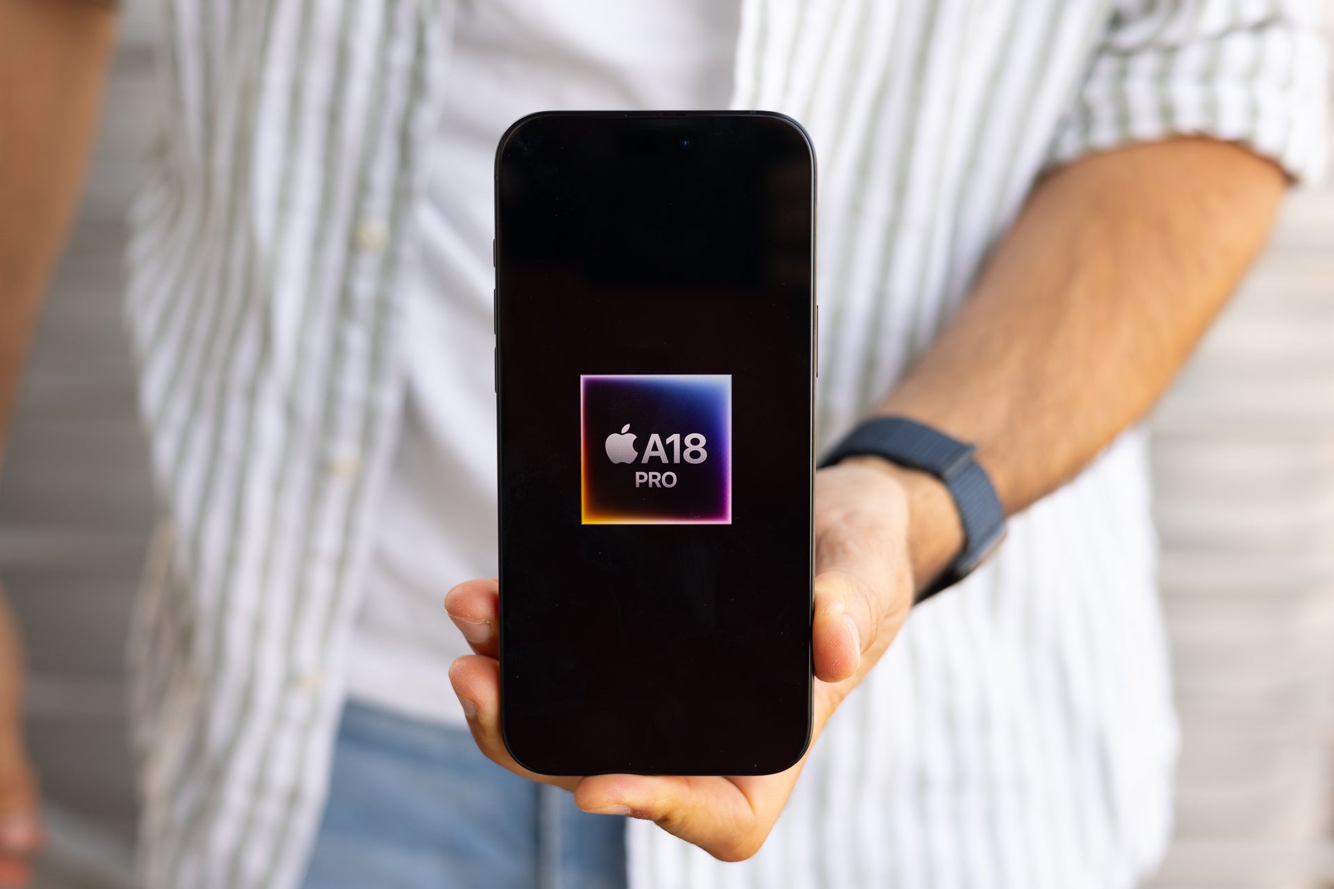 An image of a person holding an iPhone 16 Pro Max displaying the A18 Pro chip logo