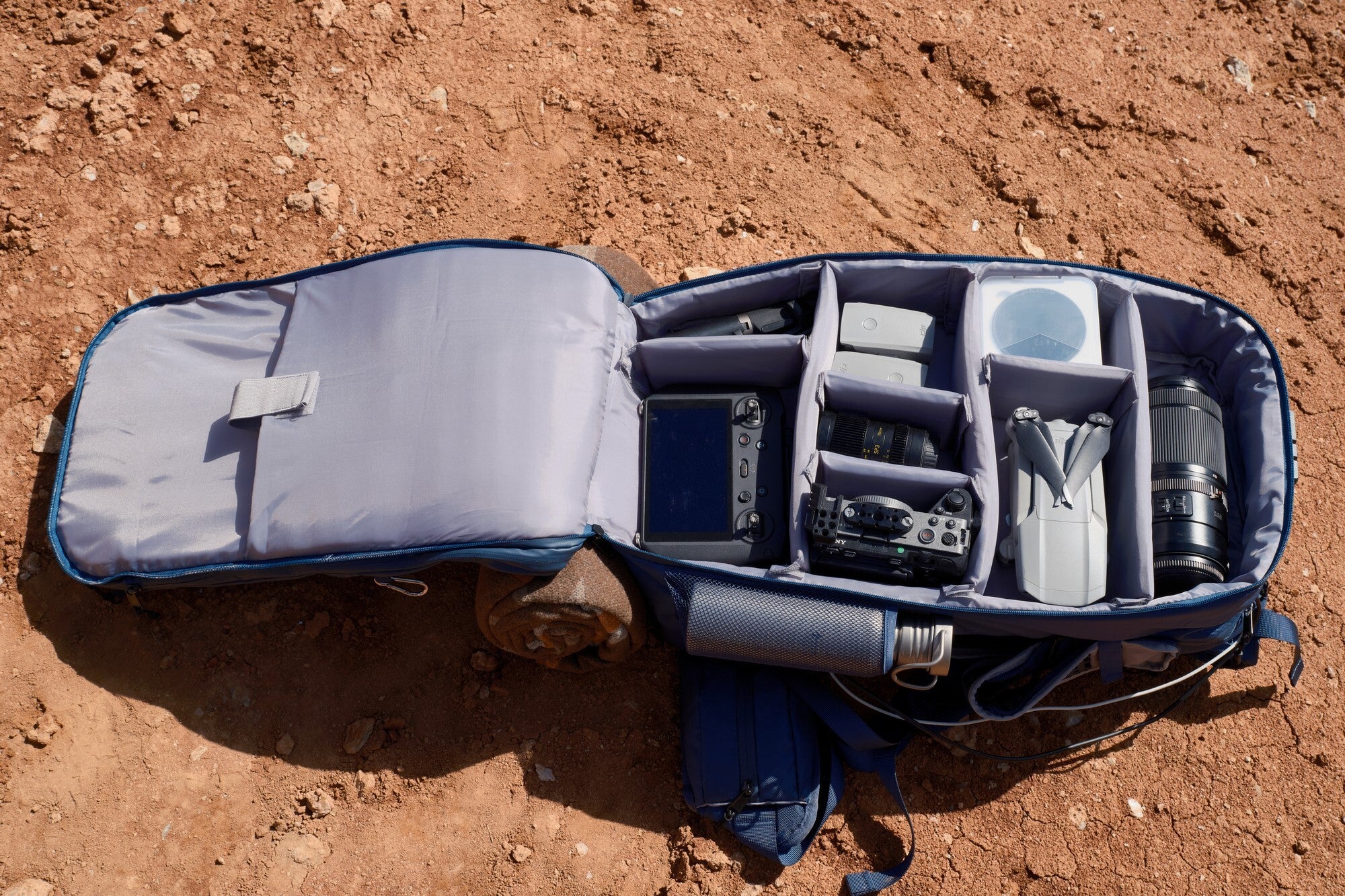 Bluetti Handsfree 2 Backpack, opened on the ground, organized with camera gear and lenses in separate compartments.