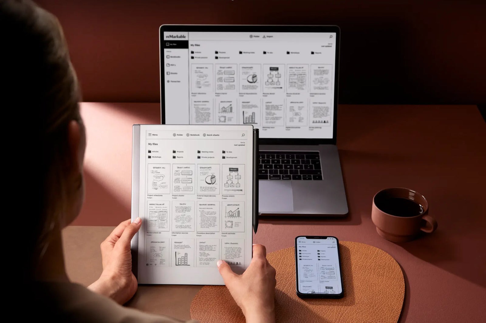 Person holding the reMarkable 2 next to their smartphone and laptop, syncing their work notes