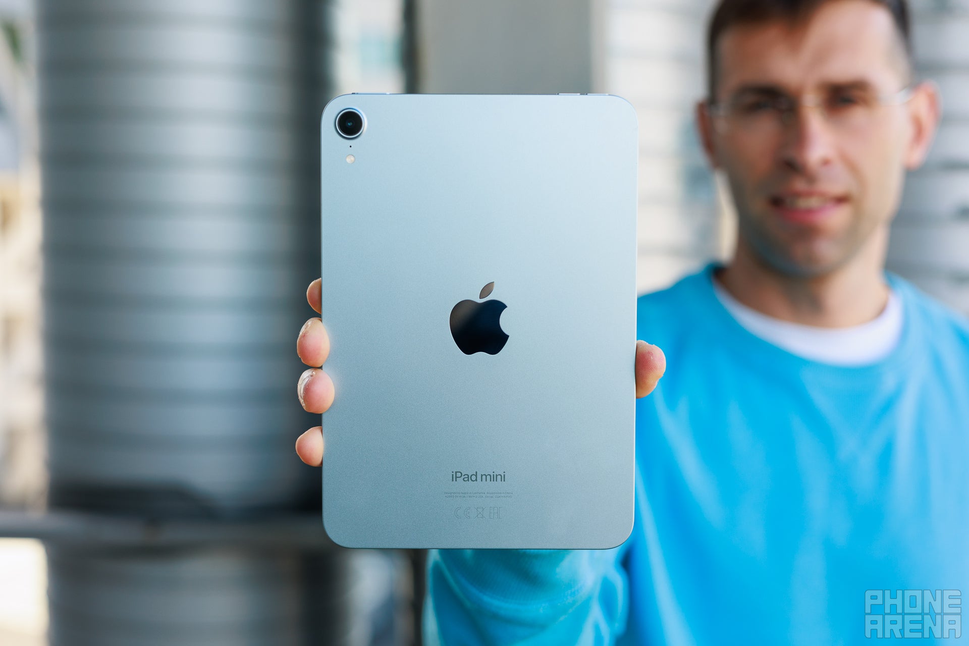 Person holding iPad mini with its back towards the camera. Tablet in blue color, Apple logo visible