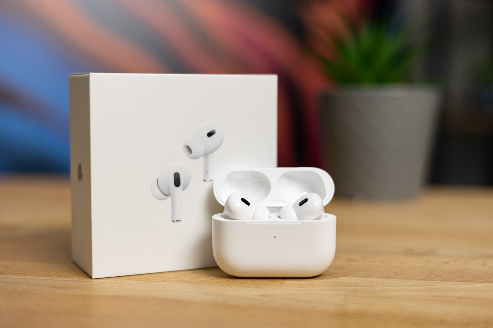 AirPods Pro 2, placed on a brown table beside their original box against a blurred background.