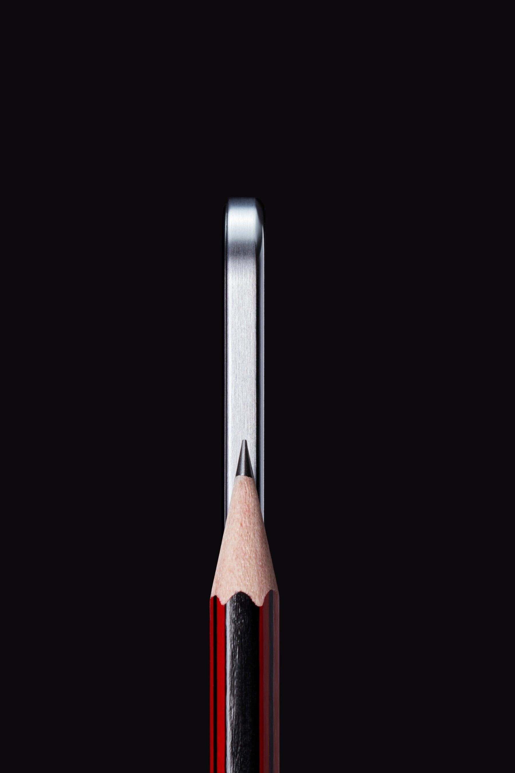 A close-up of a sharpened pencil tip aligned perfectly with the edge of a smartphone.