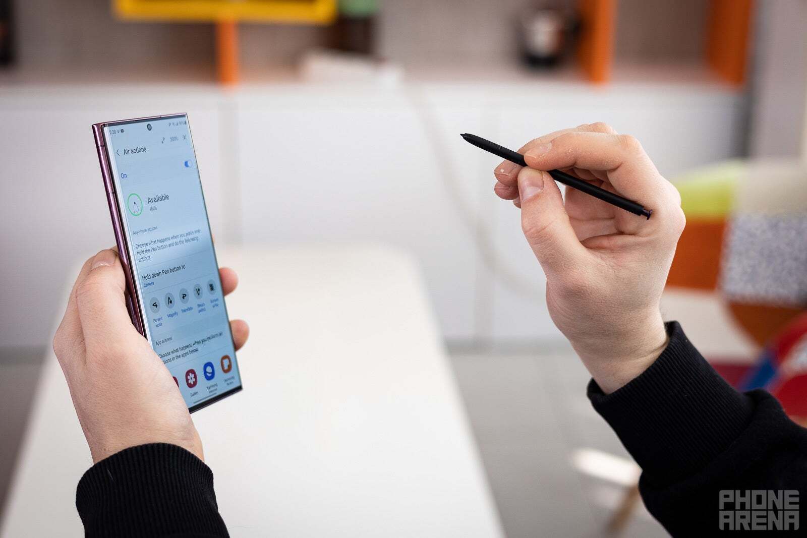 A person holding the Galaxy S22 Ultra in one hand and its S Pen in other hand. 