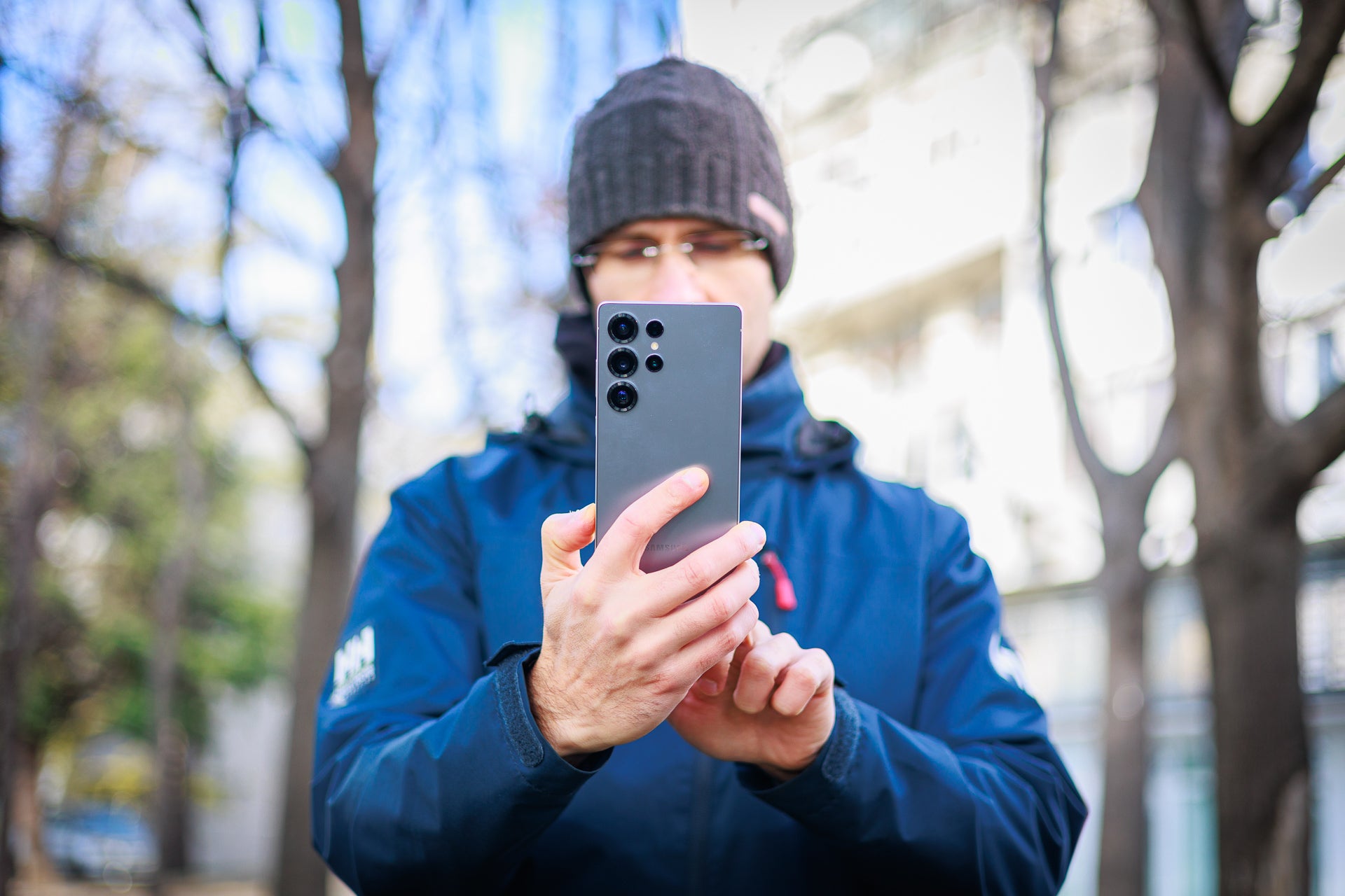 Man in the centre of the frame, holding and using a phone.