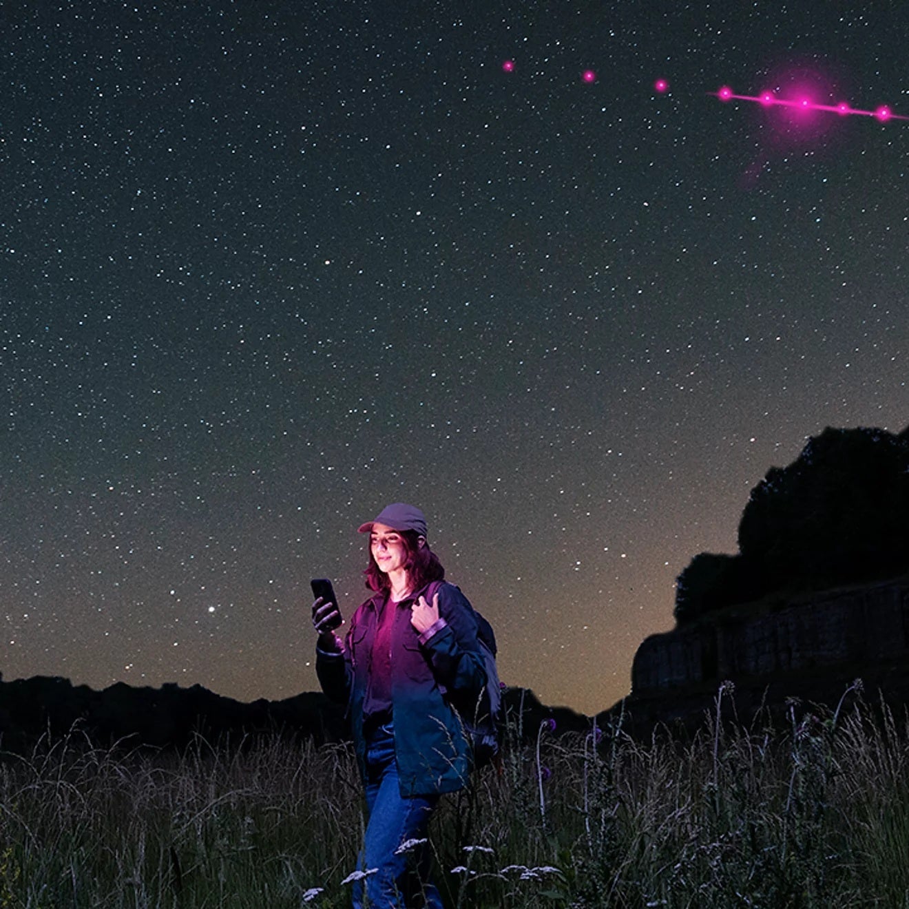 A person walking with a smartphone in hand under the starry sky.