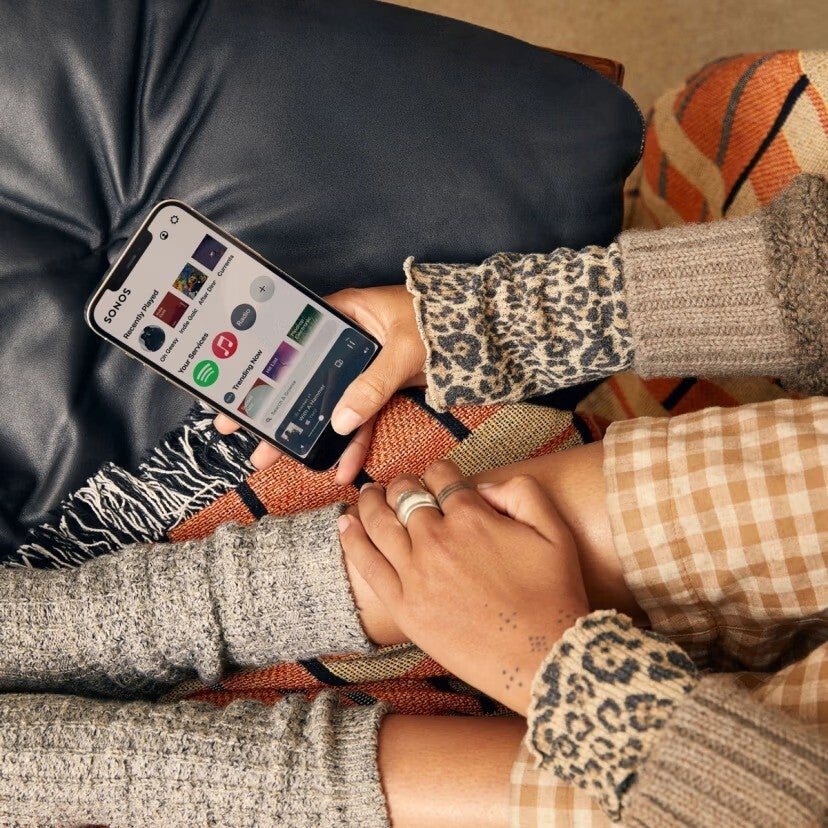 A person holding a smartphone with the Sonos app opened on it. 
