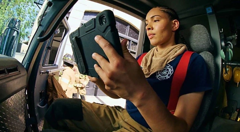 Policewoman looks at her tablet inside her police car while on the job.