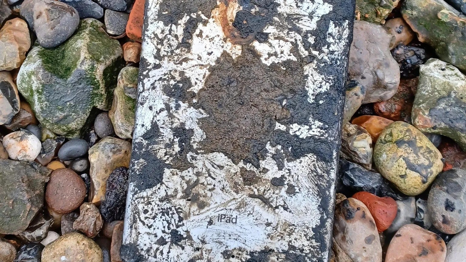 A close-up of a damaged iPad lying among rocks and pebbles.