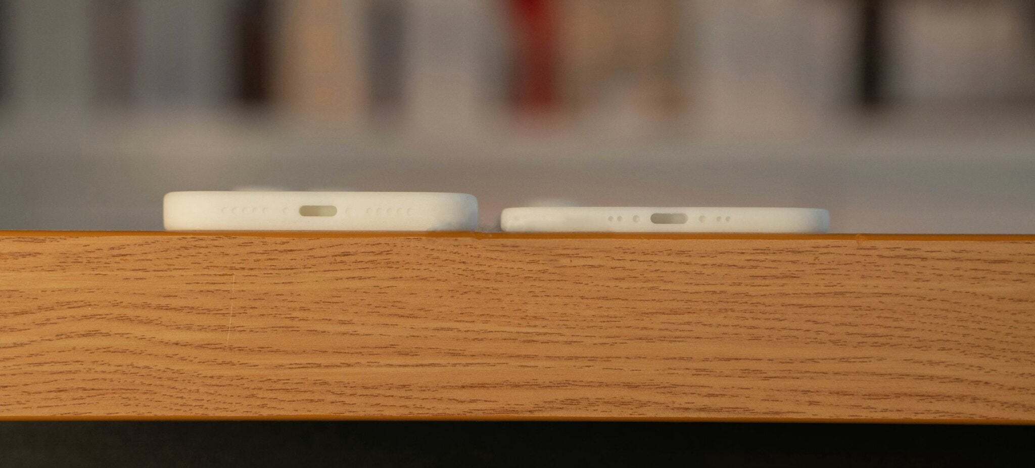 A close-up shot shows the bottom edges of two white iPhones resting on a wooden surface.