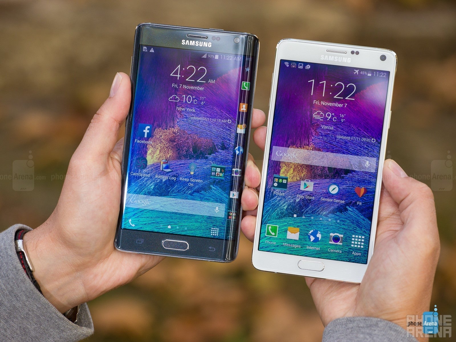 Samsung Galaxy Note Edge e Galaxy Note 4, mantidos na mão, telas em direção à câmera. Eles estão ligados, mostrando as telas residenciais com papéis de parede roxos
