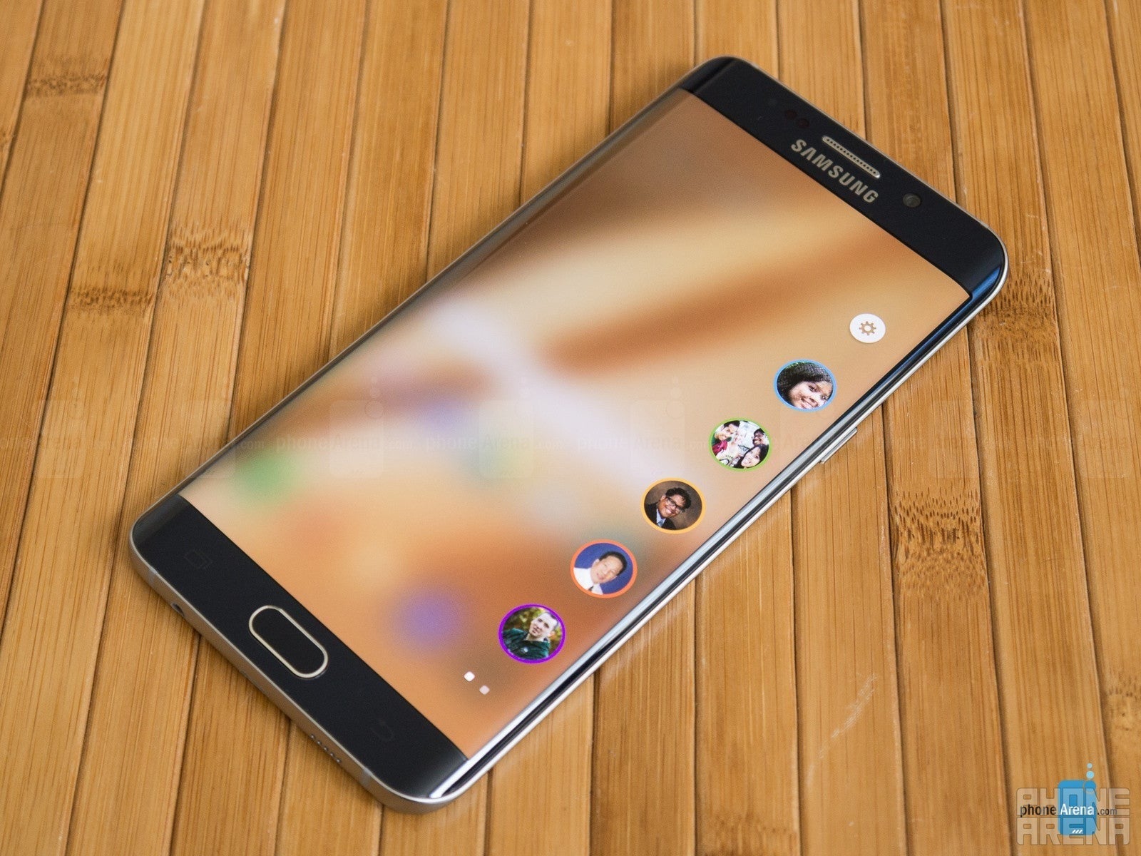 Samsung Galaxy S6 Edge+, deitado em uma mesa, a tela está ligada e um painel de borda com contatos favoritos é puxado na tela