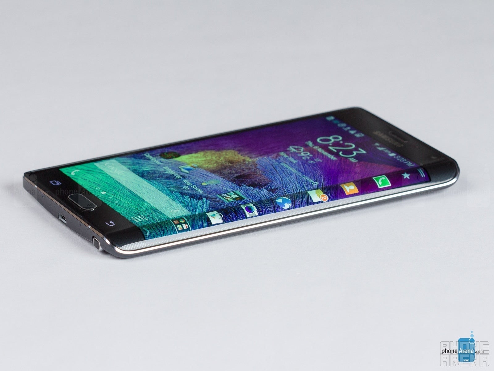 Galaxy Note Edge deitada em uma mesa, vista de lado onde a tela se curva. O telefone está ligado, mostrando a tela inicial e a barra lateral do lançador de aplicativos no lado curvo.