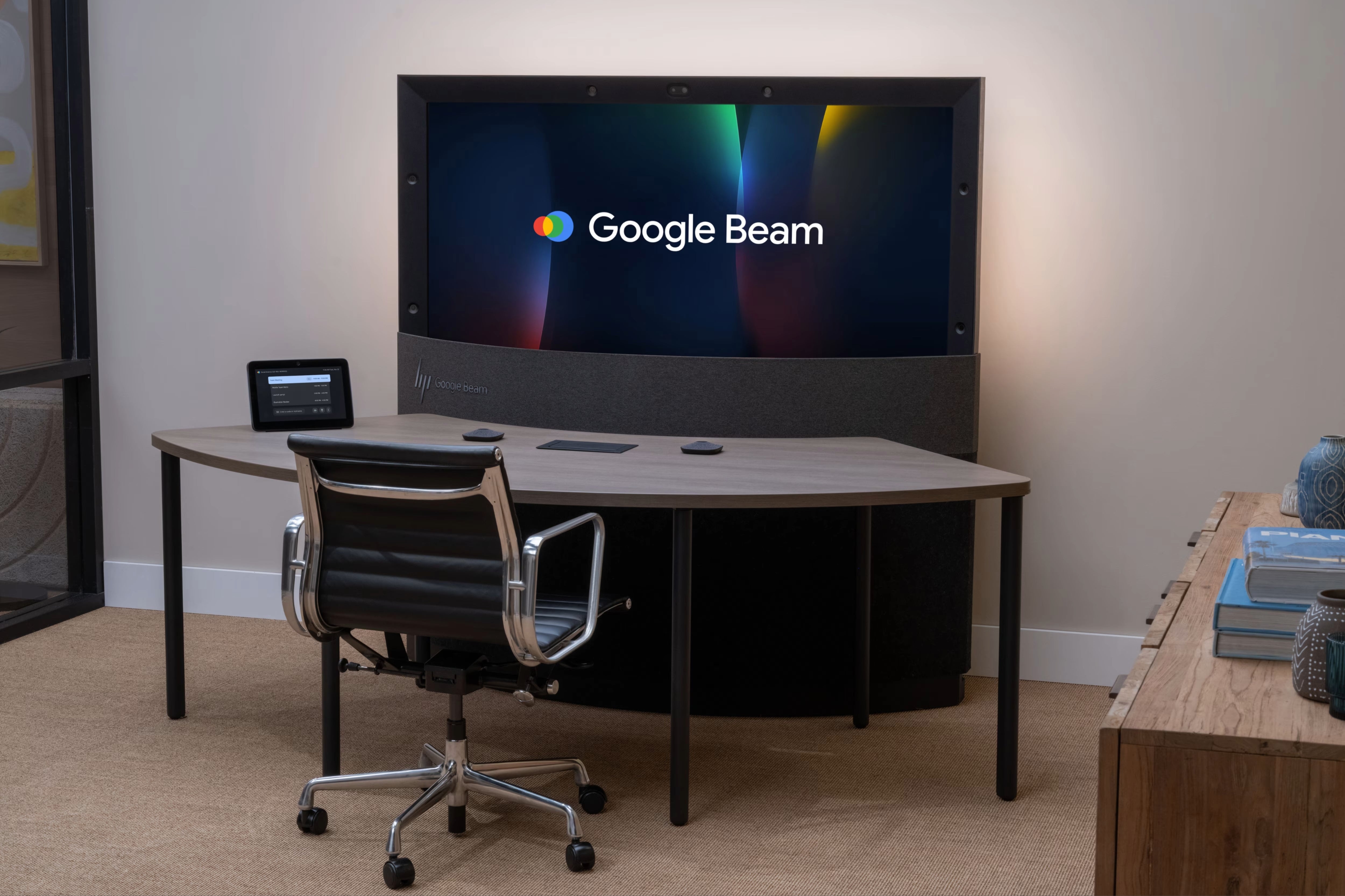 A modern office setup features a large screen displaying the Google Beam logo.