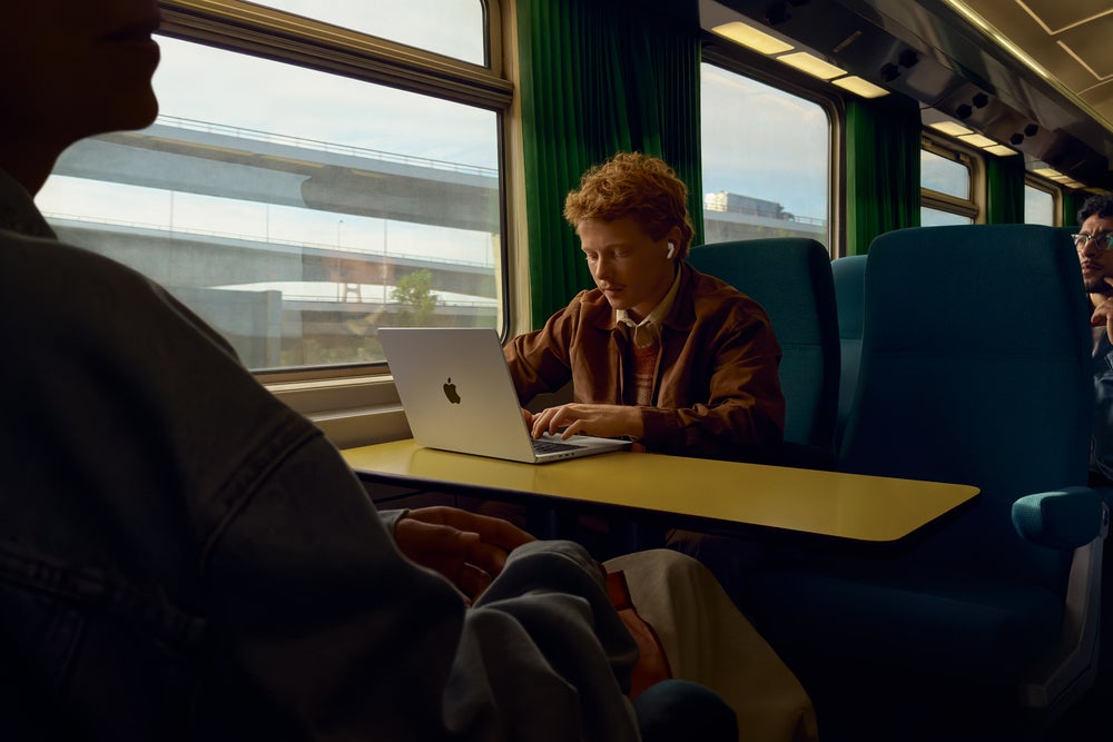 Image of man in a train using a MacBook and AirPods