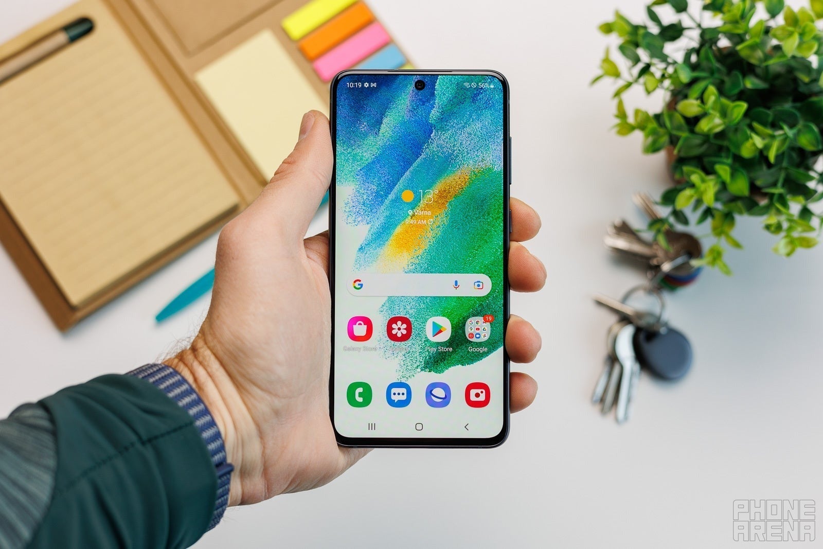 Person holding a Samsung Galaxy phone showing its home screen.