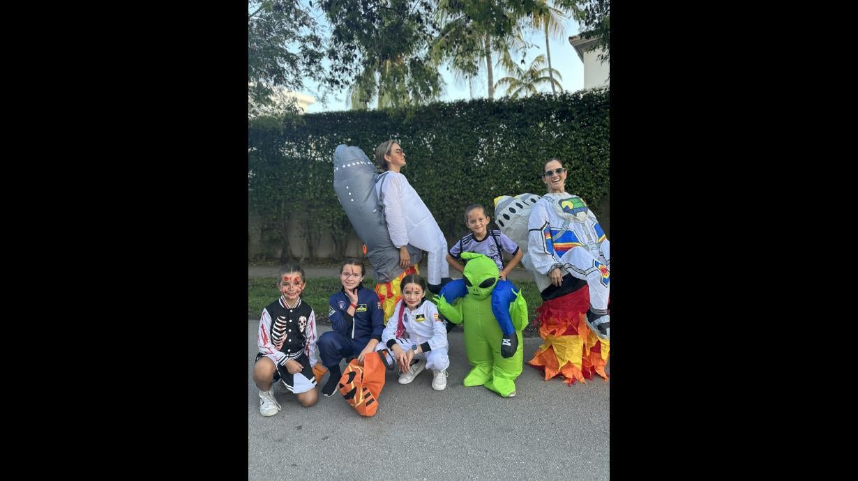 A bunch of kids in Halloween costumes on the street in daylight.