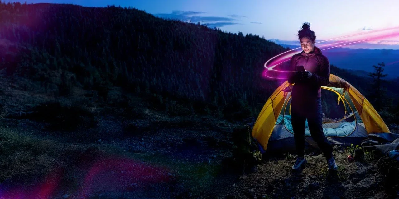 A person holding their phone outside of a tent in the great outdoors.