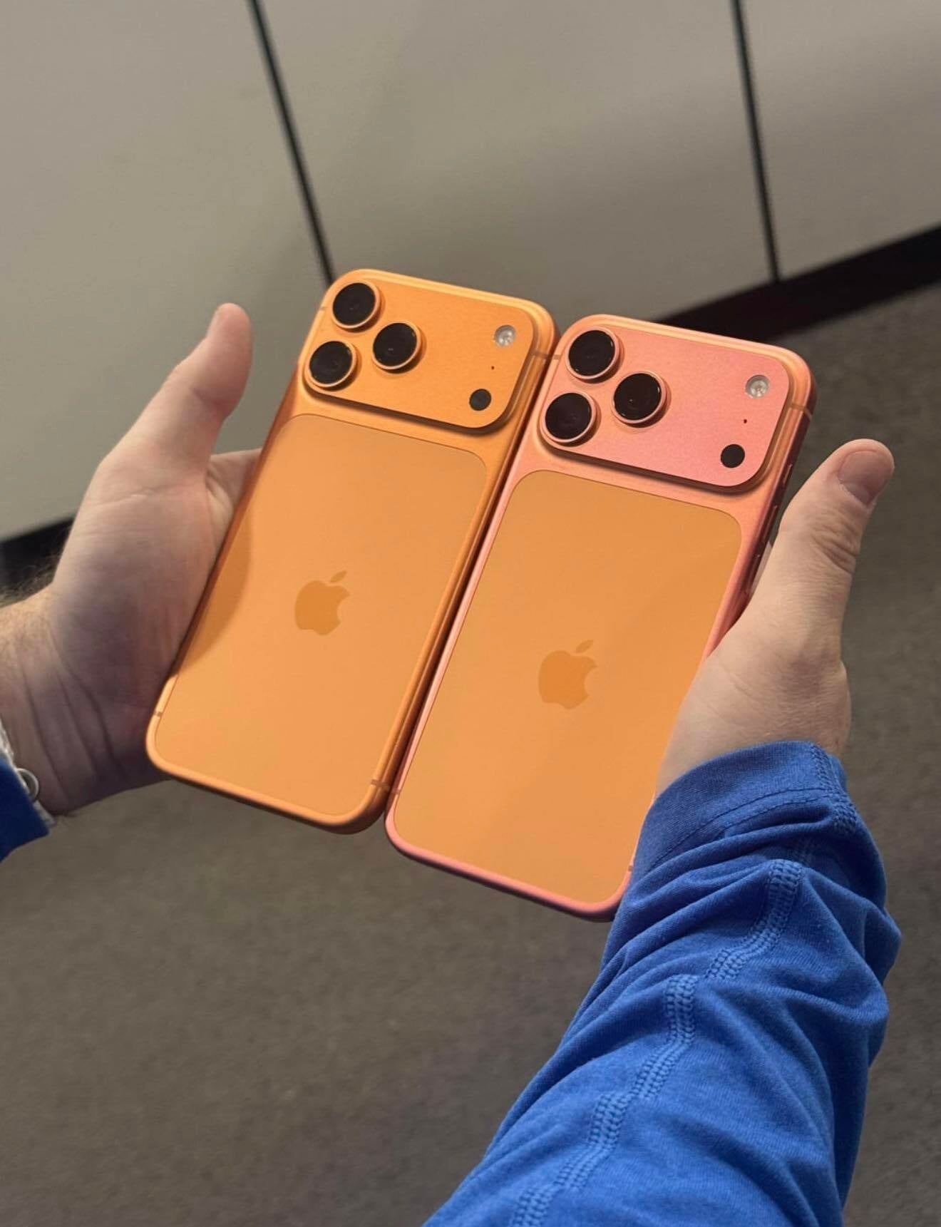 A photo of two hands holding two iPhone 17 Pros models in Cosmic Orange. 
