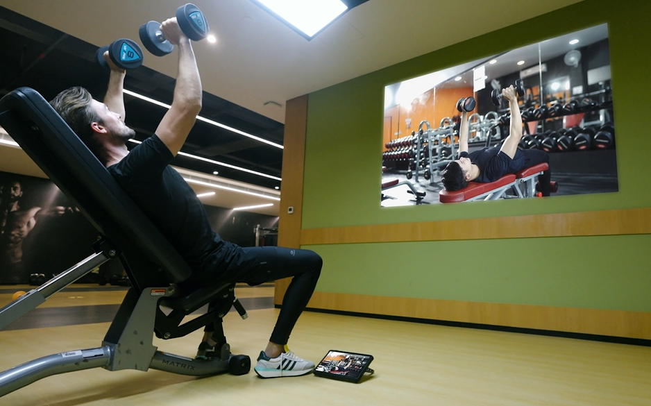 A man working out and watching a projection from the tablet.